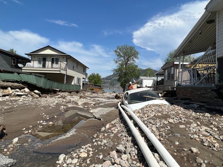 A road is pictured significantly damaged, with puddles of water, buried cars and debris everywhere.