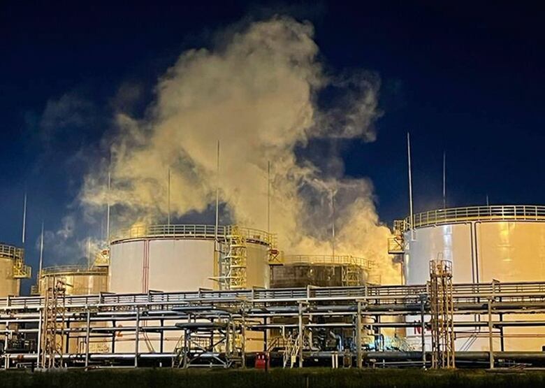 Smoke rises from an industrial sight with a darkened sky in the background.