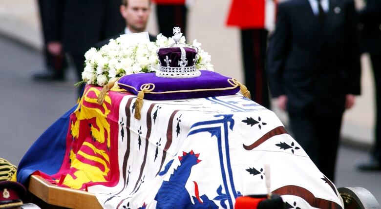 A crown with diamonds rests on a British flag on a coffin.