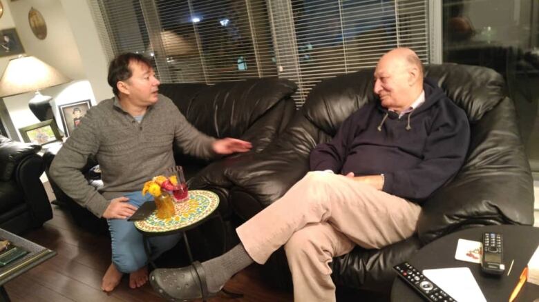 Two men sit on a leather couch and talk to each other.