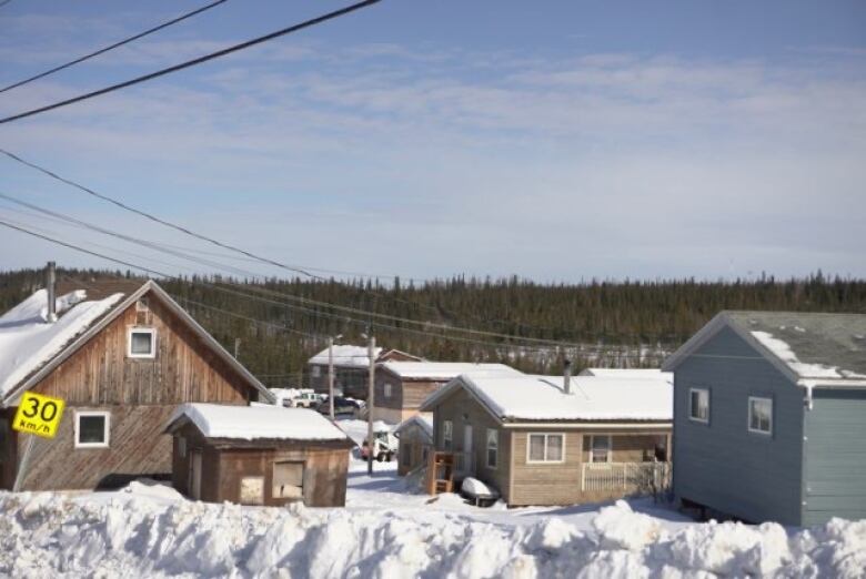 Houses on snow in front of trees in background.