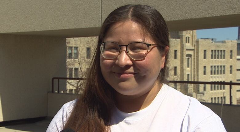 A woman with long dark hair wearing glasses smiles as she looks toward the camera.