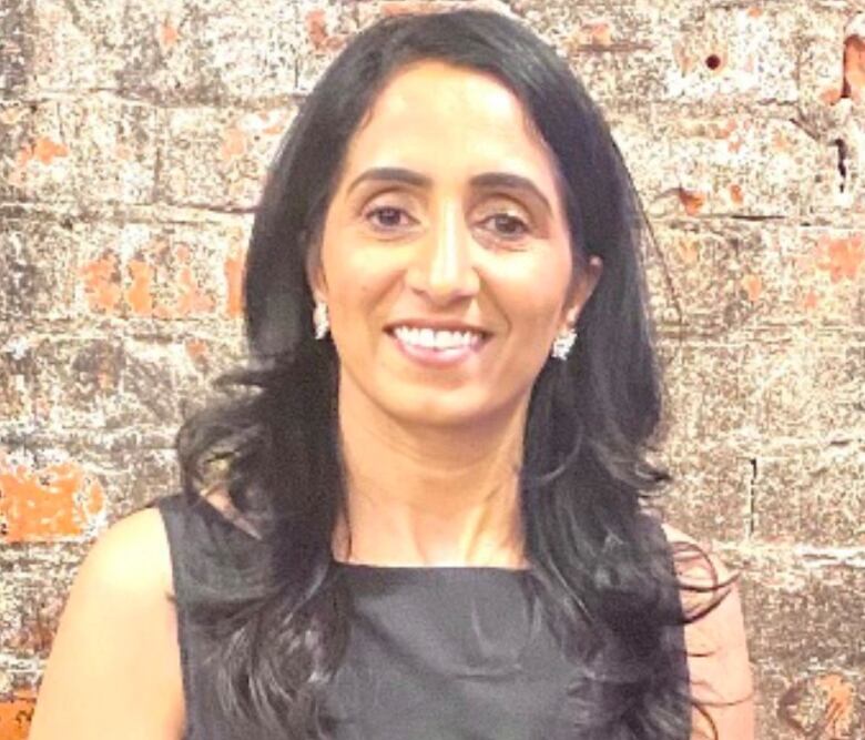 A lady wearing a black dress and sporting long hair smiles at the camera.