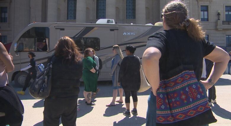 A group of people are pictured. In front of them, an RV passes by.