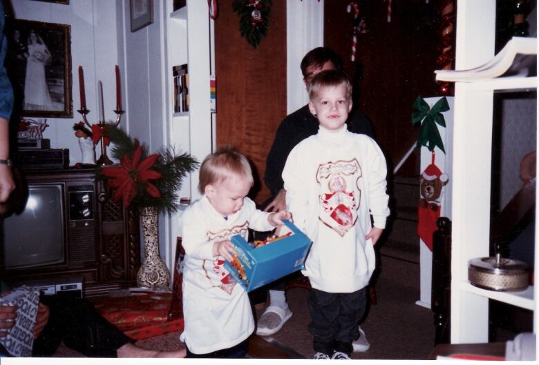 Two young boys open presents wearing oversize shirts with coats of arms.