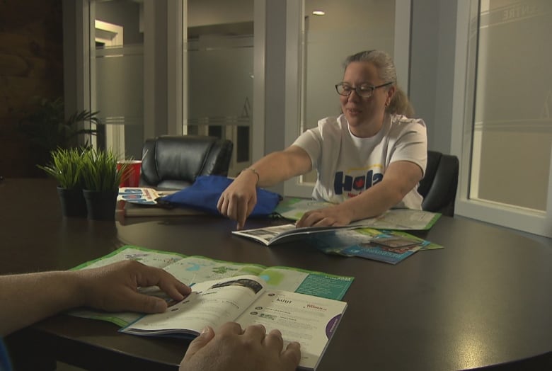 Ana Santana shows brochures and maps to a hidden asylum seeker. We just see his hands holding a booklet