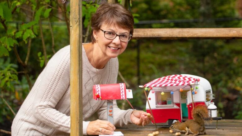 A woman leans over a small model of a camper with a squirrel in front.