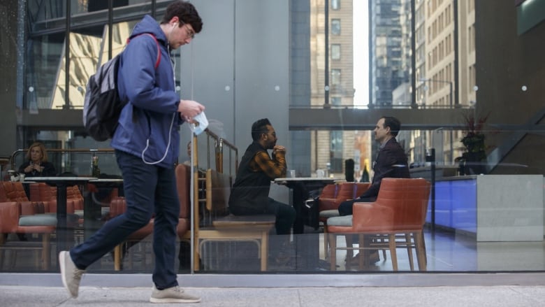 A man walks down Bay Street in Toronto while two men are shown inside the building he is walking past.