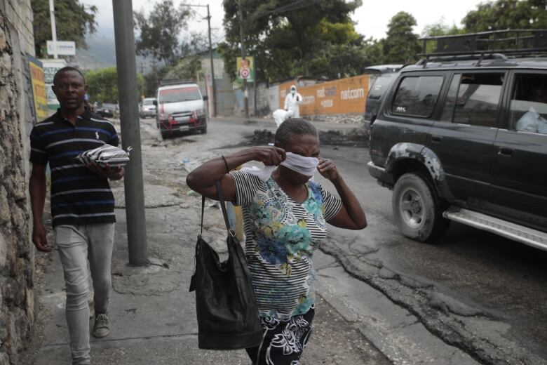 A woman walks past local authorities removing the bodies of men that were set on fire by a mob in Port-au-Prince, Haiti on April 25, 2023.