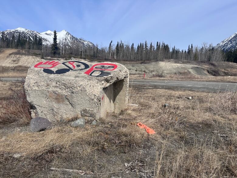 Am empty lot with a large piece of concrete decorated with Indigenous paintings. There are mountains in the background.