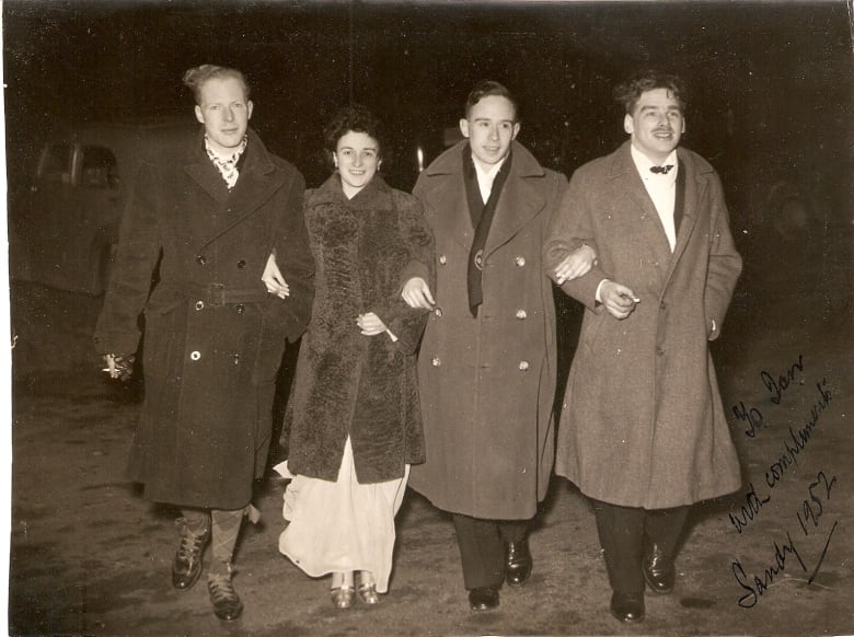 Black and white photo of four young people  three men and a woman  standing arm-in-arm.