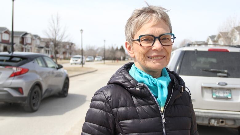 A woman posing for a photo on a road, while a vehicle drives behind her.