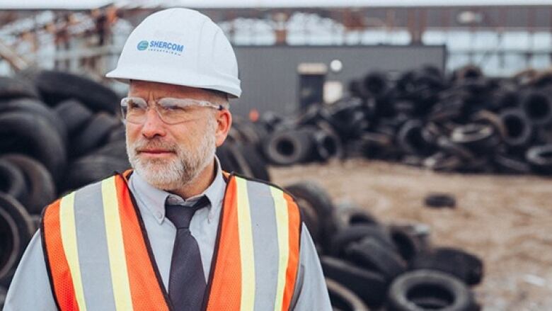 A man in a hard hat stands on a lot with tires.