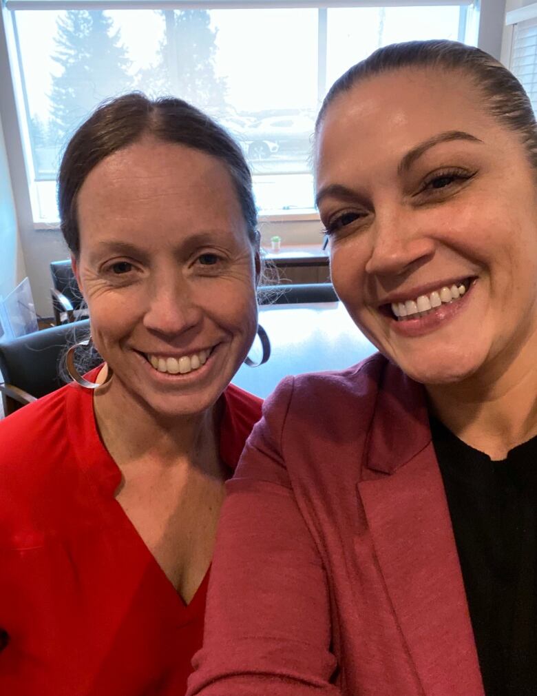 Two women wearing red smile for a picture.