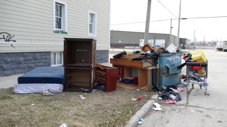 An overflowing garbage dumpster surrounded by discarded furniture and mattresses. 