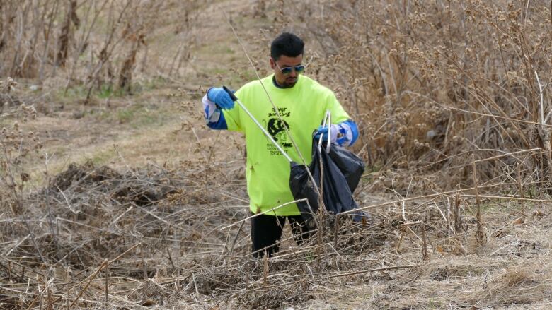 A man in blue surgical gloves and a bright t-shirt picking up litter along the riverbank. 