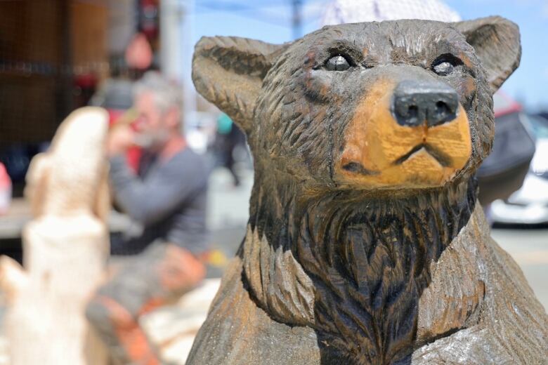 A wooden carving of a bear stands in front of the artist who created it. 