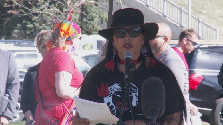 A woman wearing a black hat and sunglasses speaking at a podium.