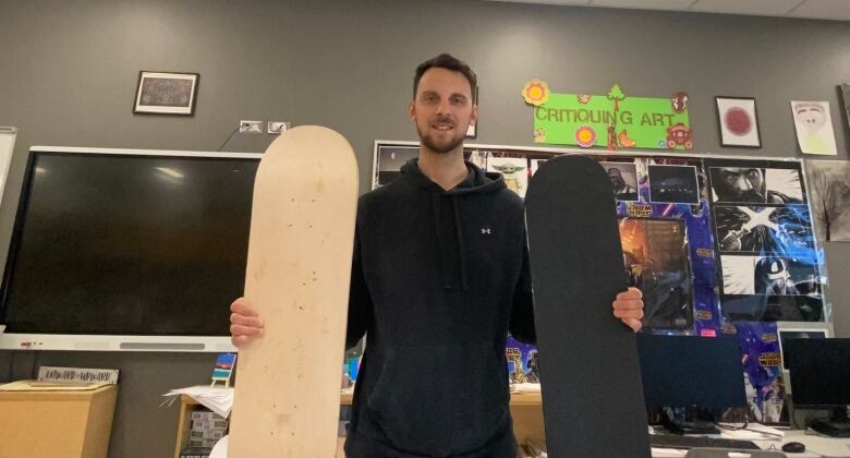 A man stands in a classroom holding two skateboards.