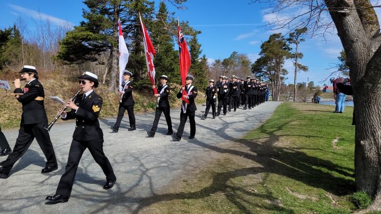 Men and women in uniform are marching and the front three are carrying flags.