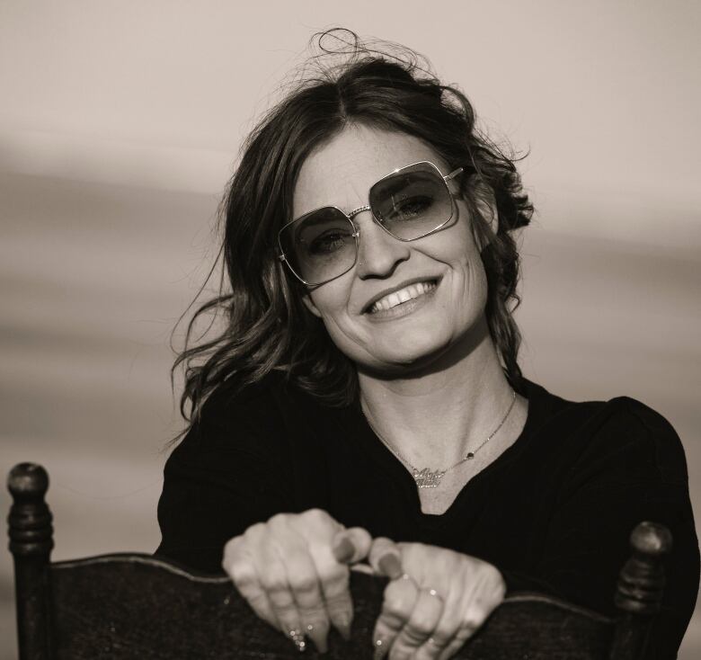 A woman in sunglasses smiles as she sits backwards on a chair.