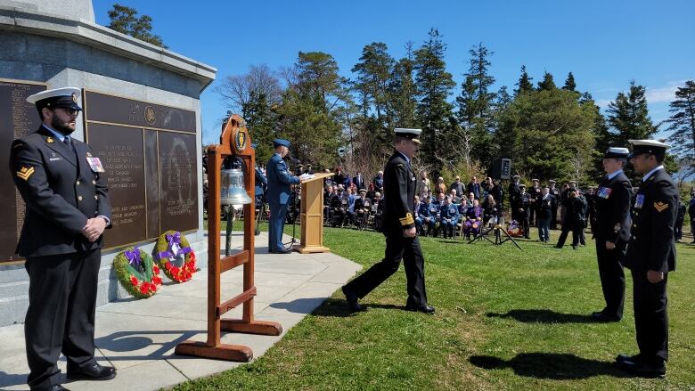 A navy commander in uniform and wearing a white hat walks away after laying a wreath at a memorial.