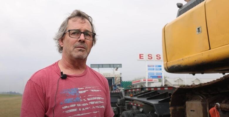 A man in a red T-shirt stands beside his truck outside a gas station.