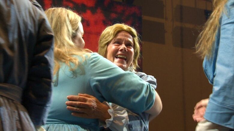 A woman in a costume for Richard Wagner's The Flying Dutchman is hugged by a chorus mate. She smiles.