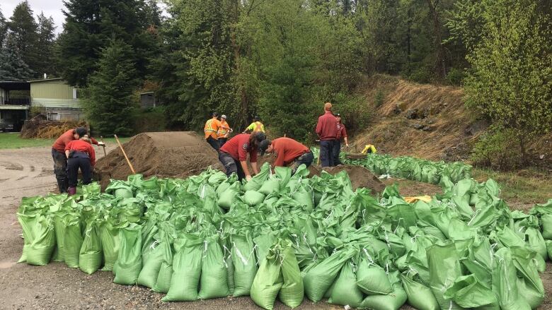 Five people pack green bags full of sand.