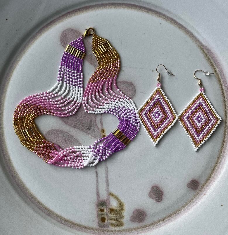 A purple, pink and gold beaded necklace lies next to a pair of diamond shaped earrings in the same shades.