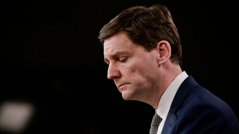 A white man wearing a suit looks down during a news conference.