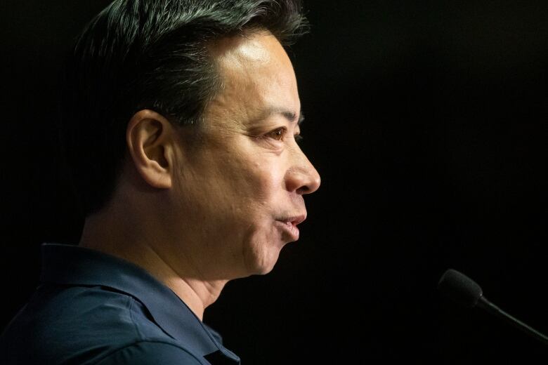 An East Asian man is pictured in profile at a news conference.