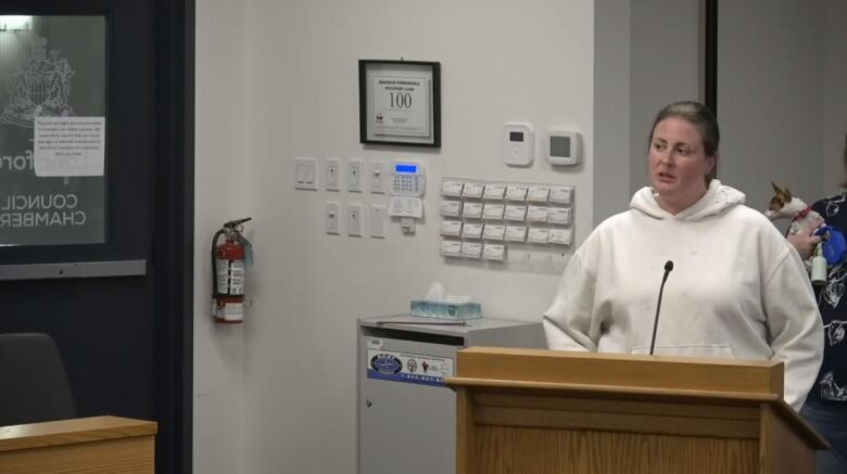 A white woman wearing a white hoodie speaks at a podium