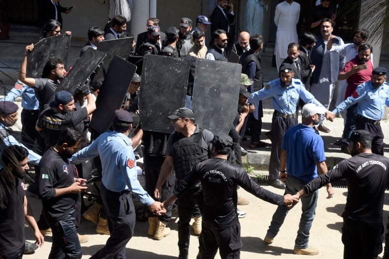 Security guards hold up large black shields around former Pakistan PM Imran Khan as he arrives to appear in court in Islamabad.