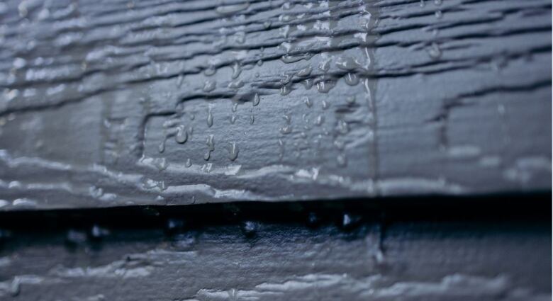 A close up of dark grey siding with water dripping off it 