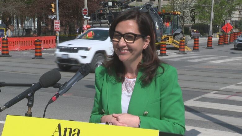 A woman in a green blazer at a podium on a city street.