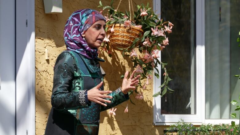 A woman in a hijab talks in front of a yellow house. 