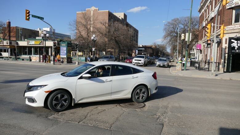 A white car is in the middle of an intersection making a left turn.