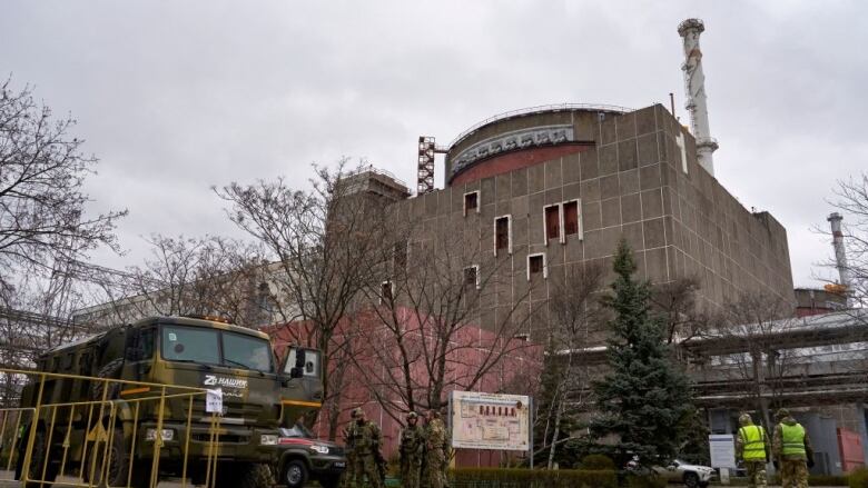 Soldiers in green uniforms stand near a green truck in front of a building at the Zaporizhzhia nuclear power plant.