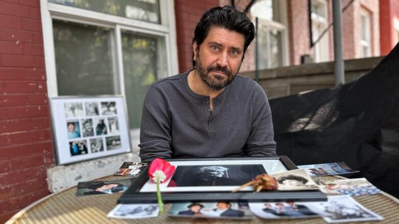 A man sits with a portrait and a flower.