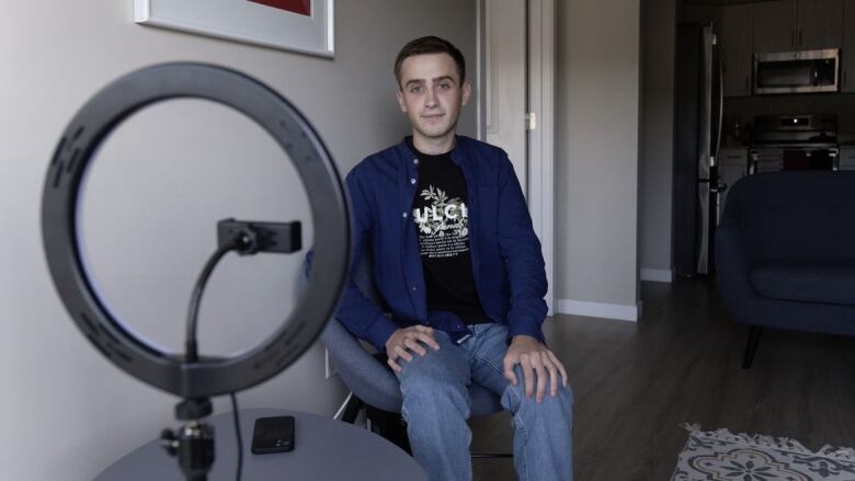 A boy wearing a blue shirt can be seen sitting on a chair and smiling. 