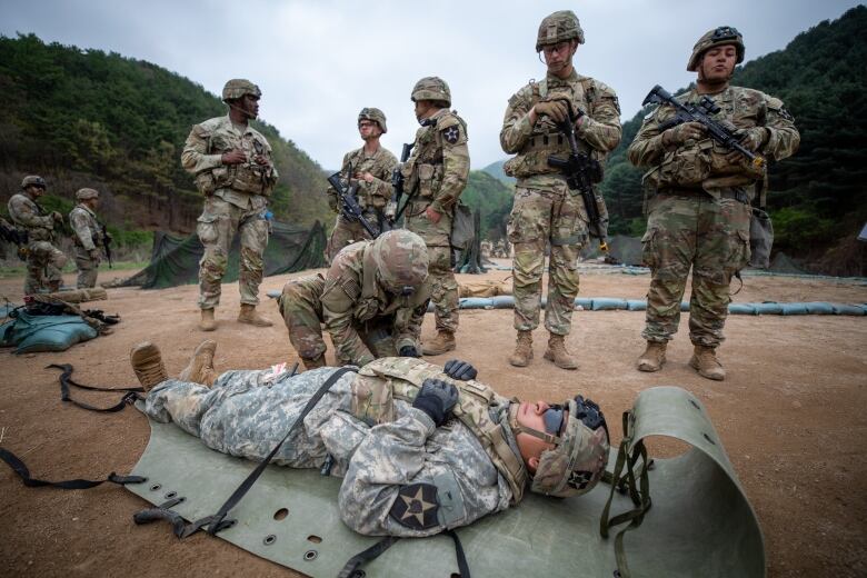 Soldiers stand around another soldier performing first aid as part of a training exercise.