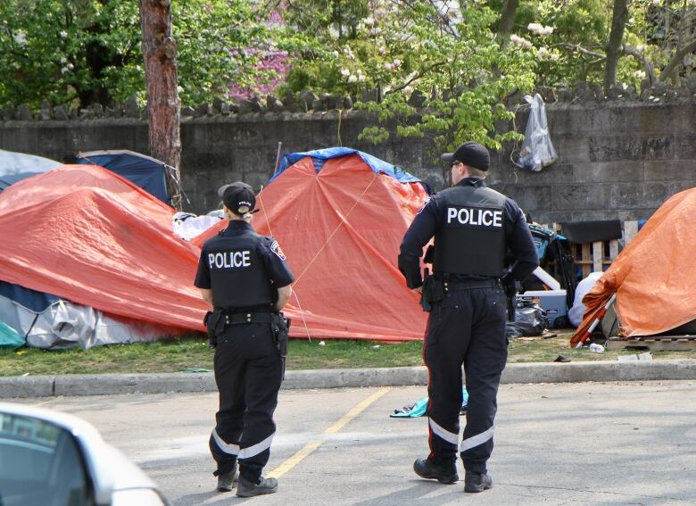 Two police officers stand in front of row of tents in parking lot