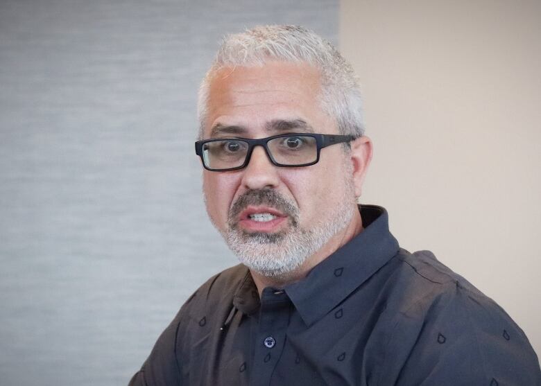 A man with salt-and-pepper hair, a dark blue shirt and glasses speaks.