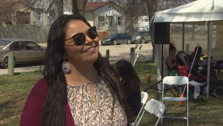 A woman in a burgundy sweater and floral print top speaks with media.