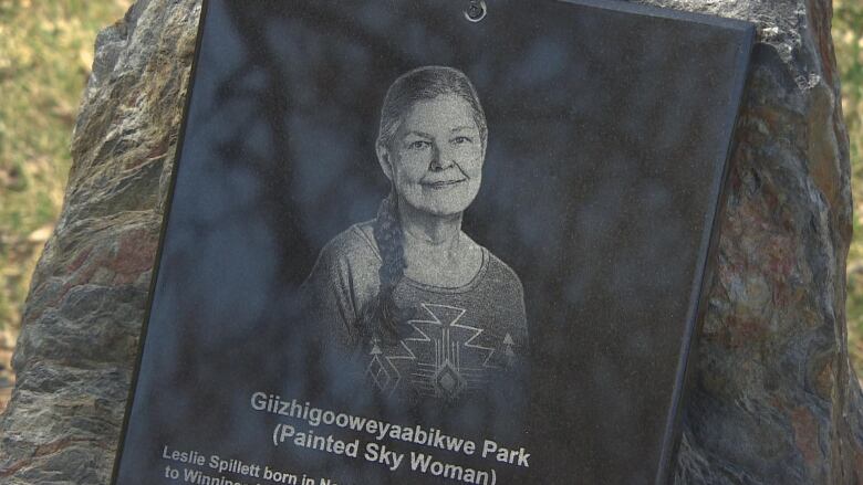 A stone monument in a park shows a woman and the Anishinaabemowin name Giizhigooweyaabikwe Park.