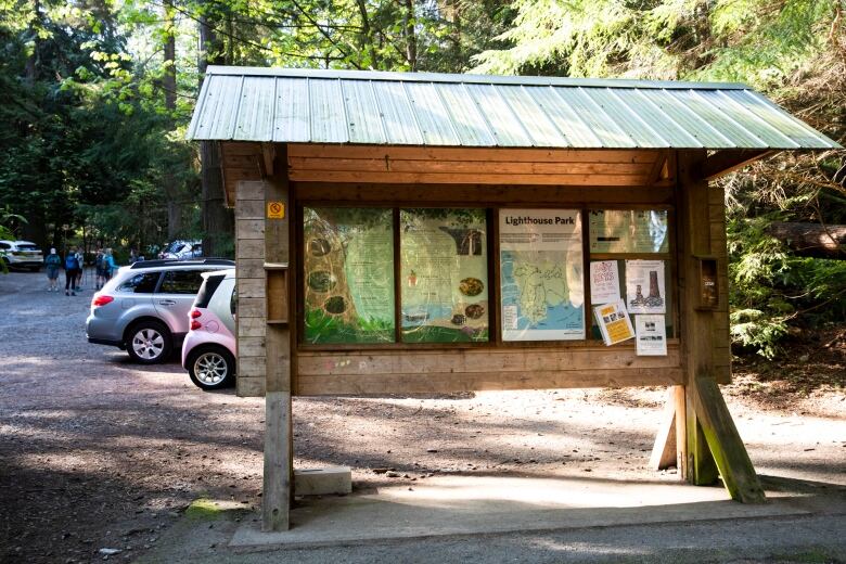 A wooden park information board with a peaked roof is seen, with cars parked in the background.