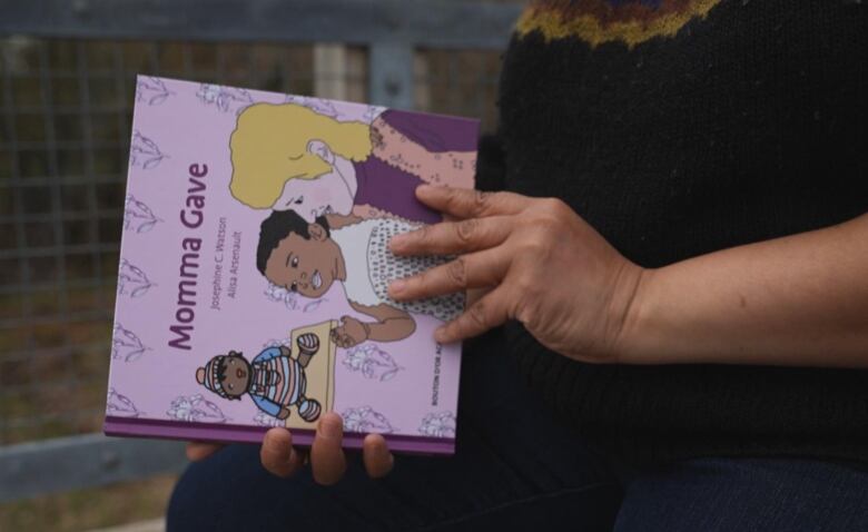 Woman holds a children's book with an illustration of her and her mother on the cover. 