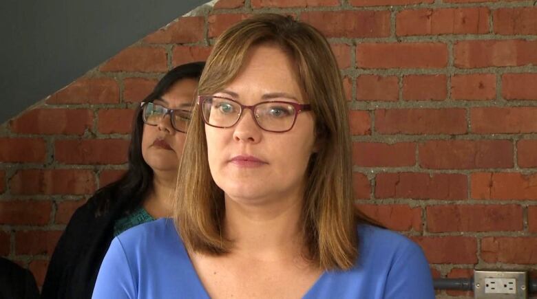 A woman stands in front of a brick wall.