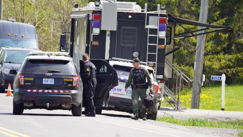 A pair of police officers walk in front of several police vehicles on a sunny day.